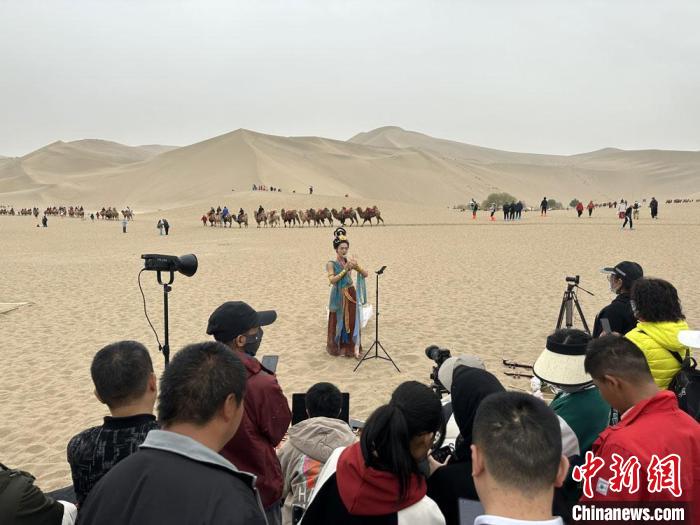 圖為2023年4月底，敦煌大漠“逐舞者”奧楠在鳴沙山月牙泉景區(qū)視頻直播，吸引游人圍觀?！●T志軍 攝