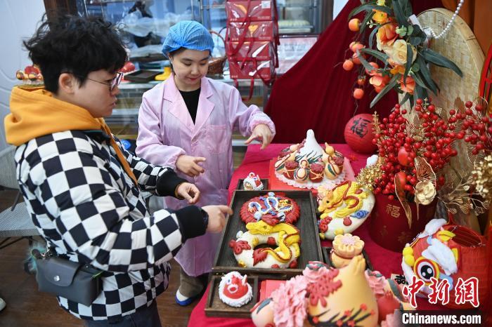 1月25日，隨著春節(jié)臨近，蘭州一花饃店“龍”元素花饃熱銷。圖為工作人員向顧客推薦“龍”元素花饃。九美旦增 攝</p><p>